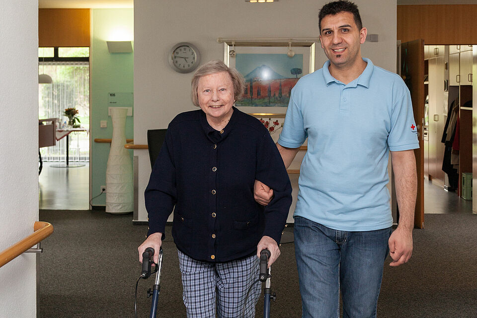 Mobiler Sozialer Hilfsdienst Ein junger Mann begleitet eine ältere Frau mit Rollator.